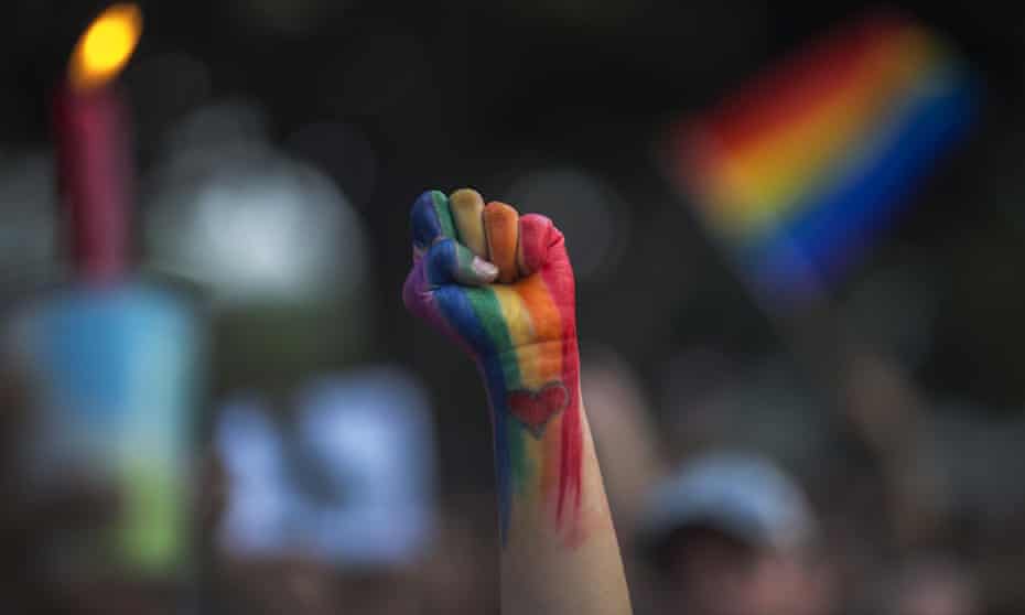 A person's raised fist painted in the colours of the LGBT rainbow flag