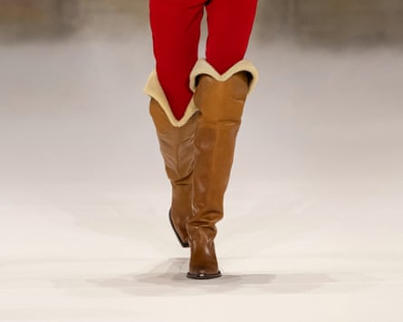 A model walks the Chloé runway in a yellow plaid blouse, red trousers and tall boots.