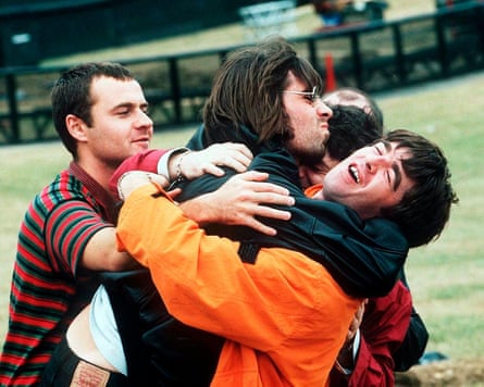The members of Oasis having a rough-and-tumble embrace in an empty field at Knebworth 1996