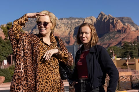 Two woman stand in a craggy landscape, one of whom wears a leopard print ensemble.