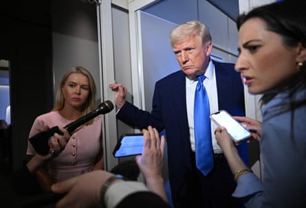 Trump stands in a doorway, listening, with reporters crowded around him
