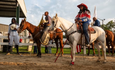 People on horses wait outside an arena