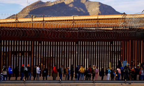 Migrants queue near the border fence, after crossing the Rio Bravo river, to request asylum in El Paso.