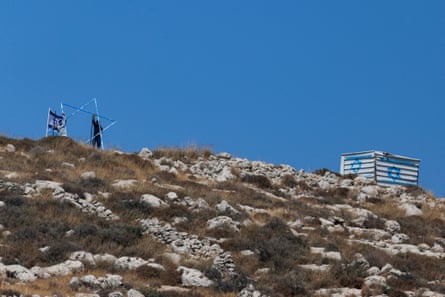 Men stand on a rocky hillside to position a large metal star and Israeli flag. To the side of them is a corrugated iron container with the blue star sprayed on its sides.
