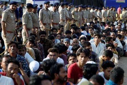 A line of police officers in uniform stands alongside a crowd of civilian men