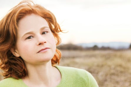 A young woman with red hair and a green jersey gazes penetratingly in an open field