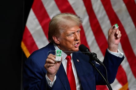Trump in navy suit and red tie holds boxes of Tic-Tacs