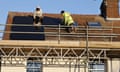 Workers installing solar panels on a roof surrounded by scaffolding.
