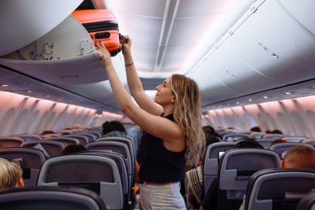 Woman putting luggage into overhead compartment on crowded plane
