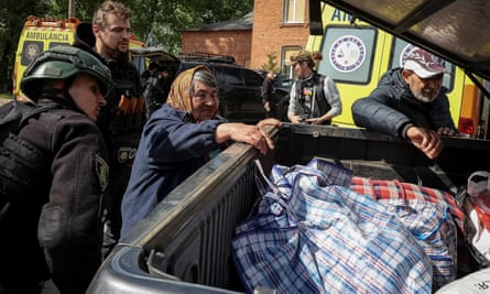 A police officer watches as people place bags in the back of a vehicle