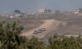 Israeli armored personnel carriers move near the Israeli-Gaza border as seen from southern Israel. Destruction in Gaza can be seen in the background