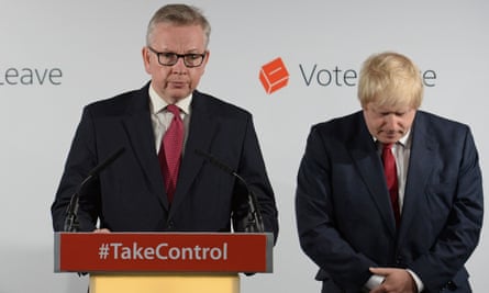 Michael Gove looking serious while standing at a lectern wearing a dark suit, a white shirt and red tie, while Boris Johnson stands next to him with his head bowed, also wearing a dark suit, a white shirt and red tie