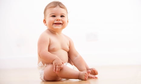 A chubby smiling baby in a nappy, sitting up