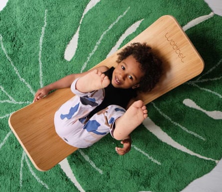 Overhead view of a child lying on their back, feet in the air, on a Wobbel Bamboo board on a rug with a leaf pattern