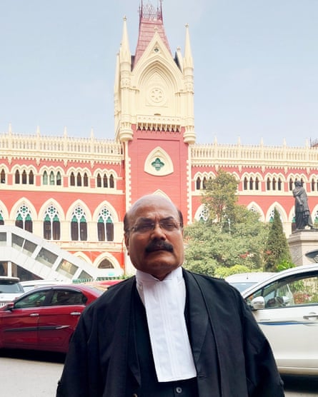 A bald Indian man wearing a lawyer’s gown standing outside an grand neo-gothic Victorian building 
