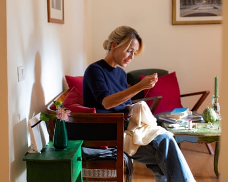 Woman sitting on sofa, darning a little cashmere sweater