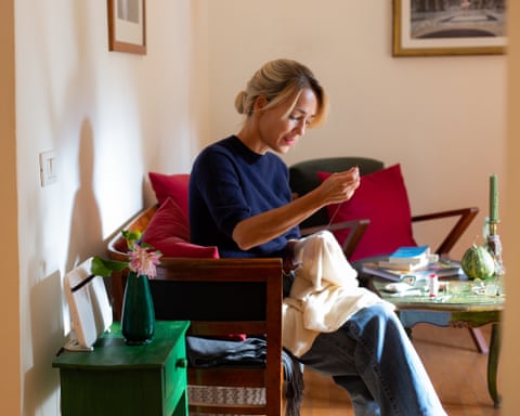 Woman sitting on sofa, darning a little cashmere sweater