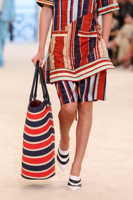 A model wearing a red, blue, green and cream striped shorts and top, carrying a large red, white and blue bag