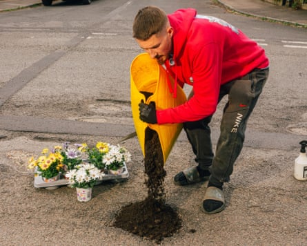 Pothole campaigner Harry Smith-Haggett, pouring soil into a pothole in the road, a tray of plants behind him
