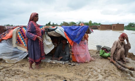 Family living in makeshift tent in mud by area of flood water.