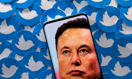 An image of Elon Musk is seen on smartphone placed on printed Twitter logos