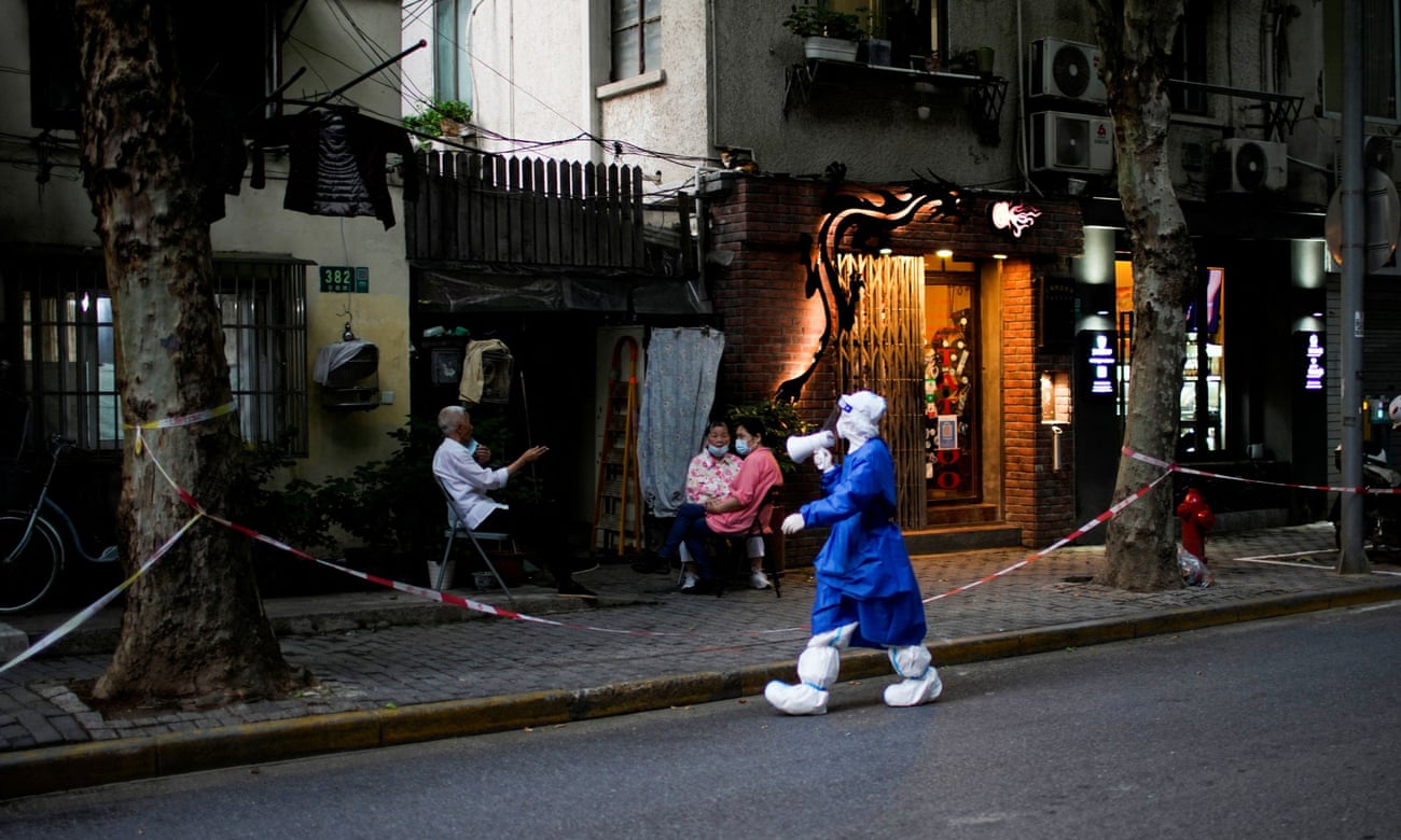 health worker in protective gear speaks to people through a megaphone