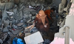 woman holds household implements surrounded by rubble