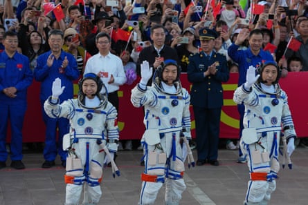 Three people in space suits wave in front of a crowd of people