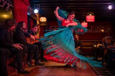 A flamenco dancer twirling in red dress with blue shawl with musicians playing next to her