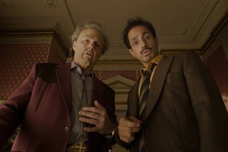 Cruise and Ahmed, in suits, stand close together with startled expressions