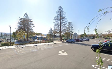 Cars park near tall trees beside a playground at a Dublin, California sports ground