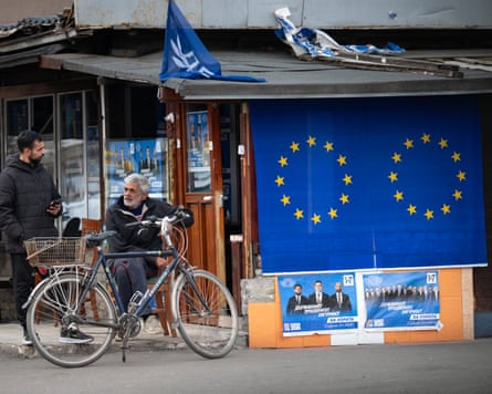 A man sits with a bike near election posters and EU flags