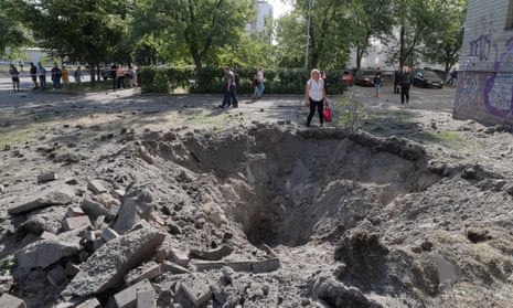 A person stands next to a shell crater on Thursday, after a missile strike in Kyiv. Three people died in the strike. 
