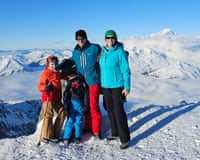 A family smiling and standing next to each other on a sunny, snowy mountaintop
