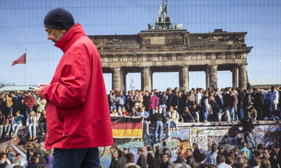 A man passes a poster from the fall of the Berlin Wall, near the Brandenburg Gate, Berlin, on German Unity Day, 3 October 2017