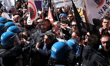 People waving flags confront police in blue helmets in a protest