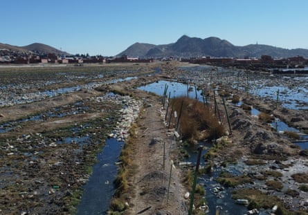 A watery ditch filled with plastic bottles and other rubbish with a settlement in the background