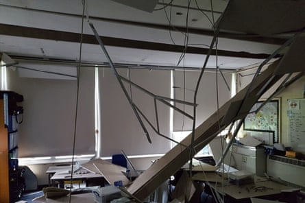 Uma sala de aula com um buraco no telhado onde um painel de concreto caiu nas carteiras abaixo