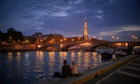 A couple sit by the river Seine at dusk in Paris, France.