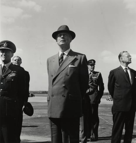 Harold Macmillan, wearing a suit and hat, stands on the tarmac at an airport with four other men standing separately, but near him