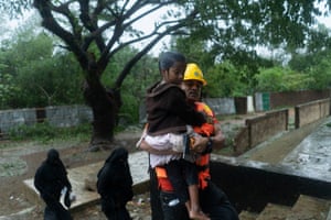 A volunteer carries a child from their house to a shelter.