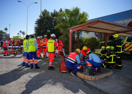 A group of people in hi-vis and hard hats stand outside. Some crouch down, they appear to be simulating a rescue