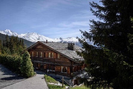A wooden three-storey chalet with snow-topped mountains in the background