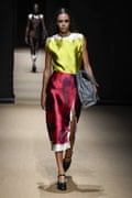 A woman in a slightly wrinkled silk top and skirt, holding a big bag on her hip