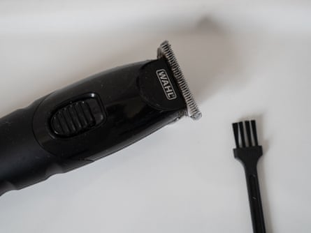 A beard trimmer with hairs in the blades next to a small brush