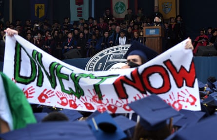 A student holds a banner that reads ‘divest now’