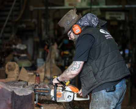 Chris Wood works on project with a chainsaw in his studio while wearing orange ear defenders