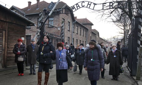 Holocaust survivors walk with others through the main gate of the former Nazi German Auschwitz-Birkenau death camp.