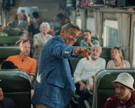 George Clooney standing in a bus full of people pointing at something in the film Jay Kelly