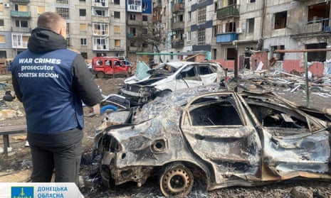 A war crimes prosecutor stands by destroyed vehicles in a courtyard of a damaged building after a missile attack in Myrnograd.